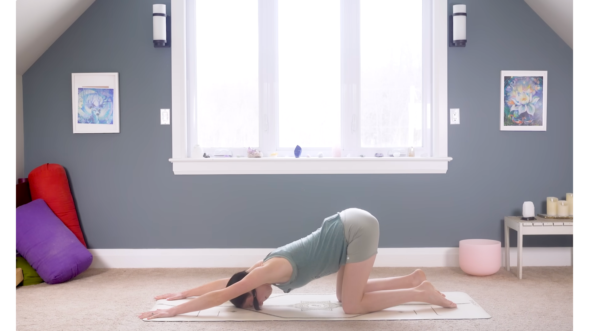 Yoga teacher kneeling on a mat in a backbend and shoulder stretch known as Puppy Pose